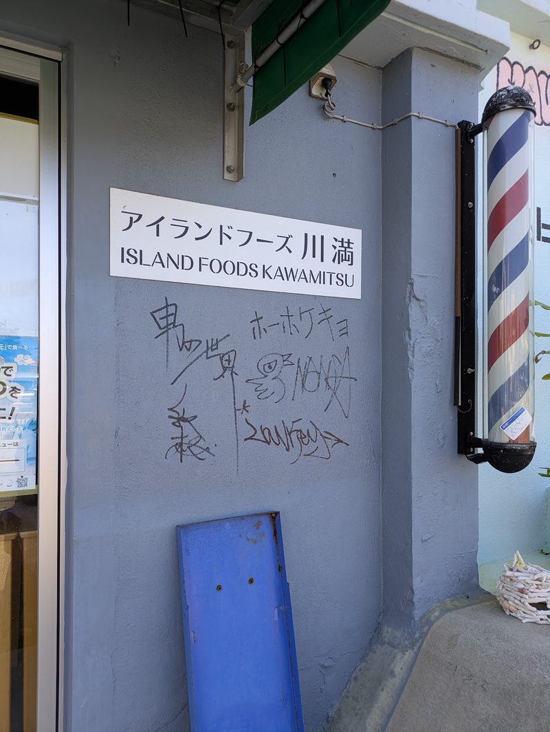 入口の壁に残る「アイランドフーズ川満」の看板とサイン